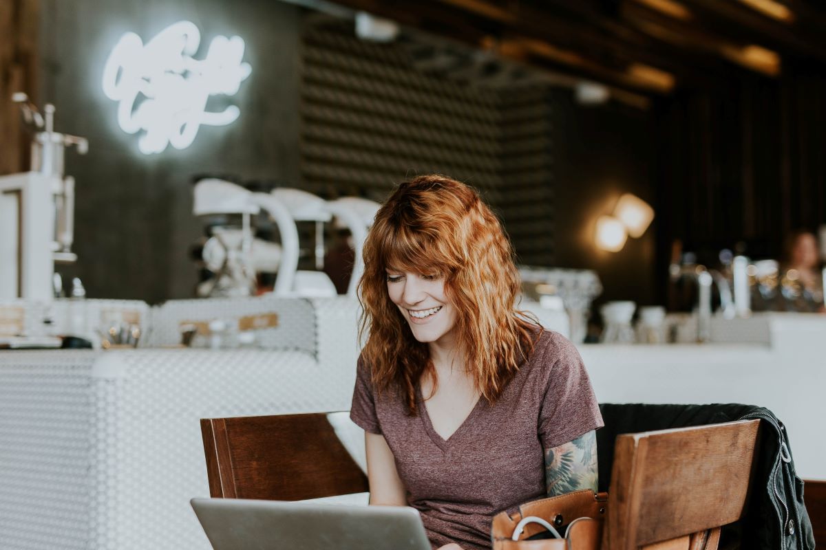 young redheaded woman with tattoos smiling at her laptop in hip office space