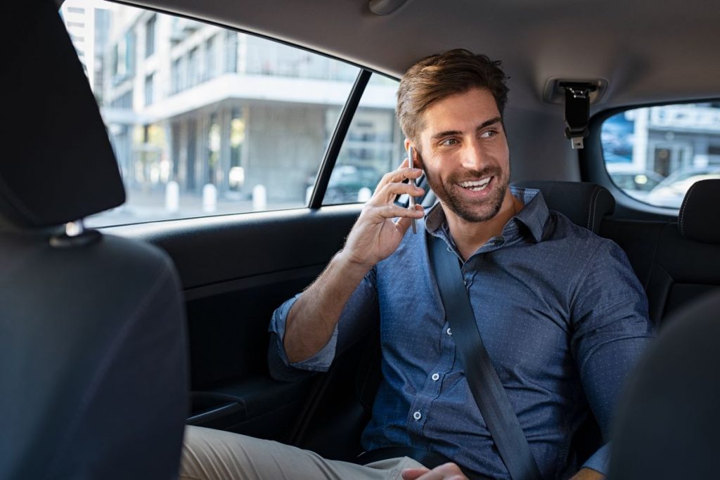 young professional man smiling while talking on cell phone in back seat of a taxi